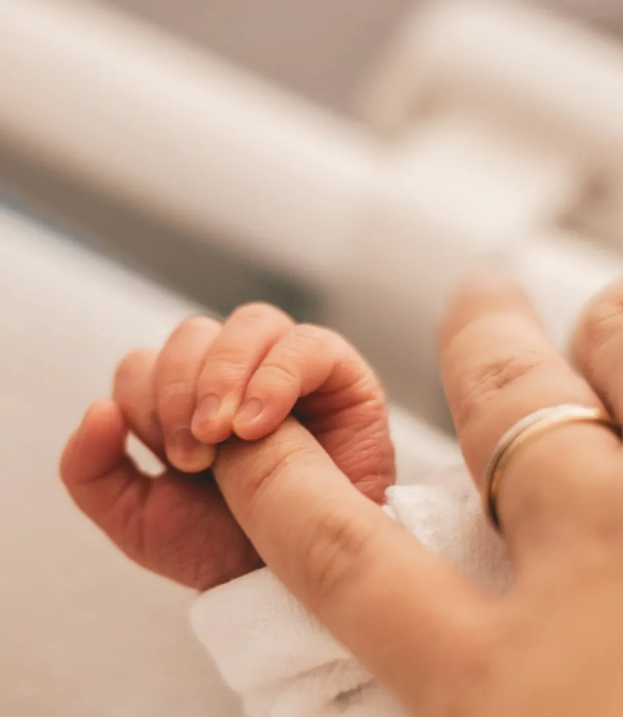 Mãos de um bebê apoiadas nas mãos de um adulto, em fotografia de referência.